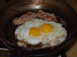 フライパン中央に卵２個と上端にベーコン２切れのフライドエッグ
