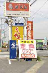 筑紫野市塔原西の中華料理屋さん「福禄飯店」。道路沿いの看板。赤に白字で福禄飯店、白に赤字で定食６５０円と書いた看板が居酒屋や、黄色のラーメンチェーン店の看板といっしょに立っています。